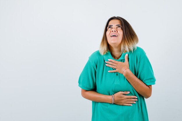 Giovane donna che tiene le mani sul petto e sullo stomaco in t-shirt polo e sembra allegra, vista frontale.