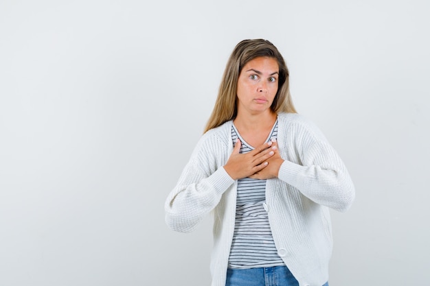 Giovane donna che tiene le mani sul petto in t-shirt, giacca e sembra perplessa, vista frontale.