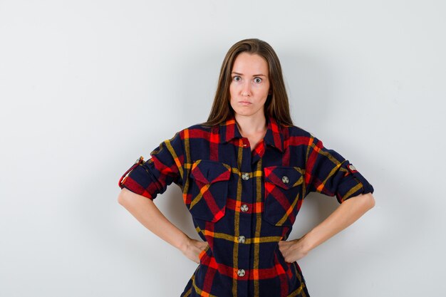 Giovane donna che tiene le mani sulla vita in camicia casual e sembra dispettosa. vista frontale.