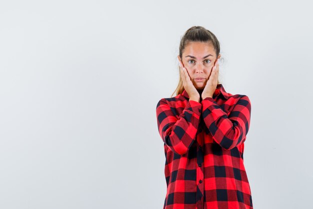 Giovane donna che tiene le mani sulle guance in camicia a quadri e dall'aspetto delicato