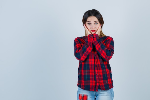 Giovane donna che tiene le mani sulle guance in camicia a quadri e sembra sensata, vista frontale.