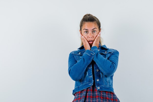 Giovane donna che tiene le mani sulle guance in camicia, giacca e guardando sorpreso. vista frontale.