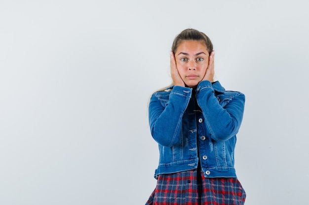 Giovane donna che tiene le mani sulle guance in camicia, giacca e sembra spaventata. vista frontale.