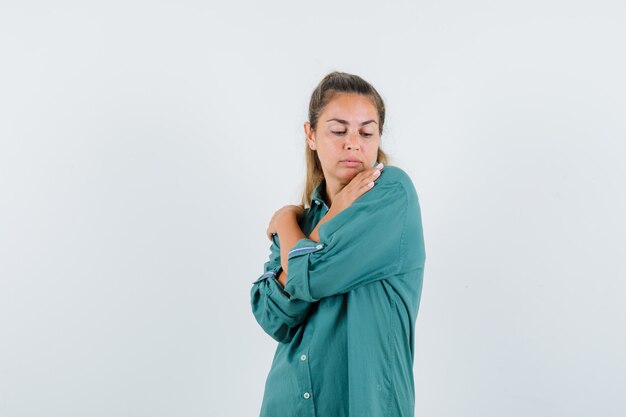 Giovane donna che tiene le sue mani incrociate sulle spalle in camicia blu e che sembra soddisfatta