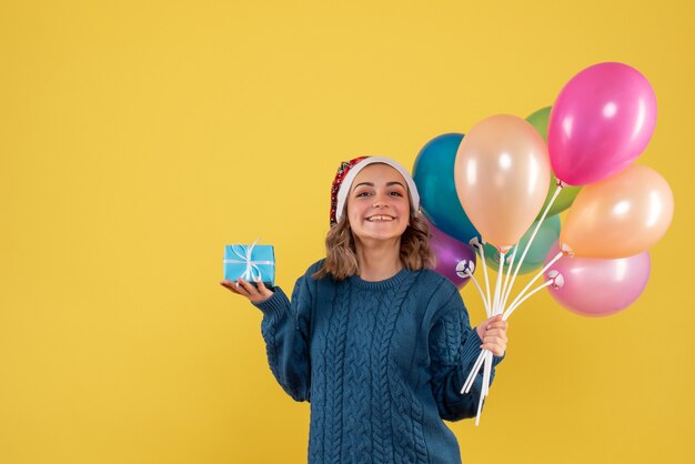 giovane donna che tiene poco presente e palloncini sul giallo