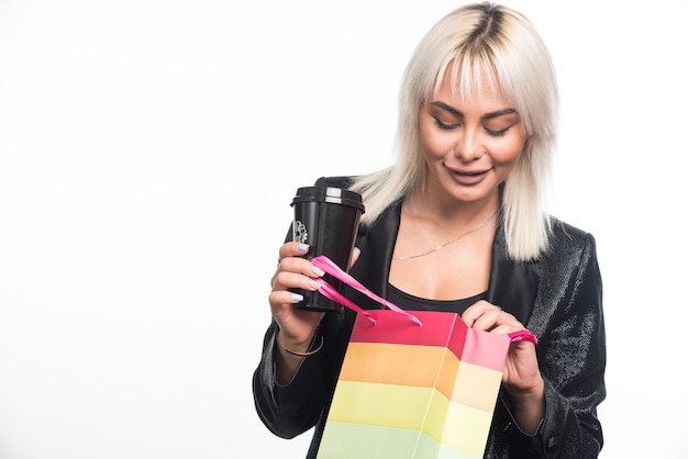 Giovane donna che tiene sacchetto regalo colorato e tazza su sfondo bianco. Foto di alta qualità