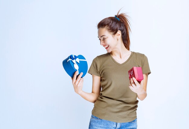 Giovane donna che tiene scatole regalo rosse e blu a forma di cuore e le gode