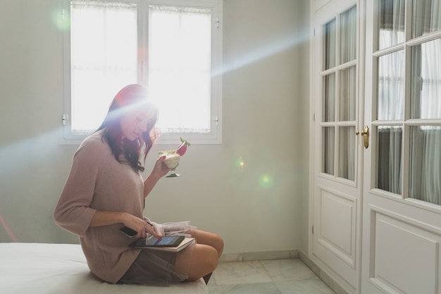 Giovane donna che tiene un cocktail e usando il suo tablet