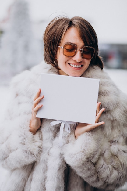 Giovane donna che tiene un contenitore di regalo bianco all'aperto