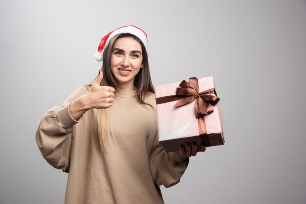 Giovane donna che tiene un regalo di Natale e che mostra un pollice in su.