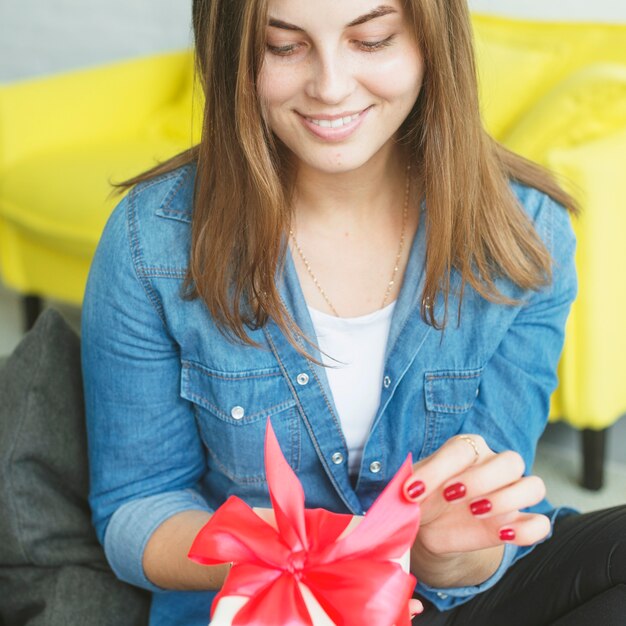 Giovane donna che tira il nastro rosso per aprire il suo regalo di compleanno
