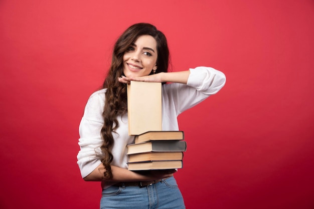 Giovane donna che trasporta libri e sorride su uno sfondo rosso. Foto di alta qualità