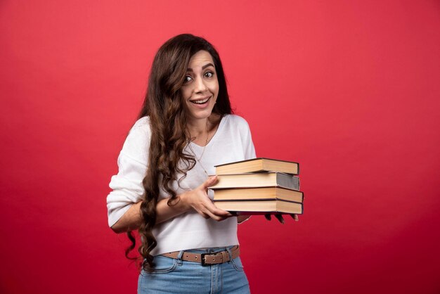 Giovane donna che trasporta libri su uno sfondo rosso. Foto di alta qualità