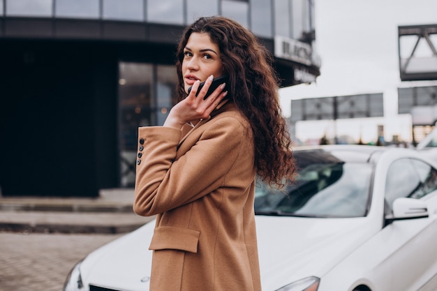 Giovane donna che usa il telefono e in piedi vicino alla macchina