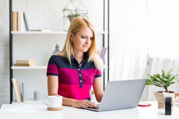 Giovane donna che utilizza computer portatile sopra lo scrittorio