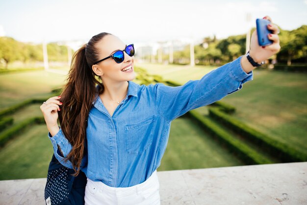 Giovane donna che utilizza il telefono cellulare prendendo selfie nel parco