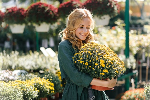 Giovane donna con bei capelli biondi e un sorriso gentile, vestita di una tunica verde con cintura sta lavorando in serra