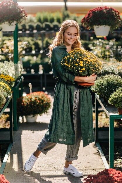 Giovane donna con bei capelli biondi e un sorriso gentile, vestita di una tunica verde con cintura sta lavorando in serra