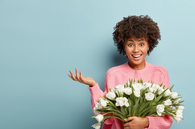 Giovane donna con capelli ricci che tiene il mazzo di fiori bianchi