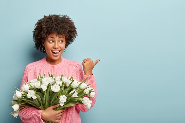 Giovane donna con capelli ricci che tiene il mazzo di fiori bianchi