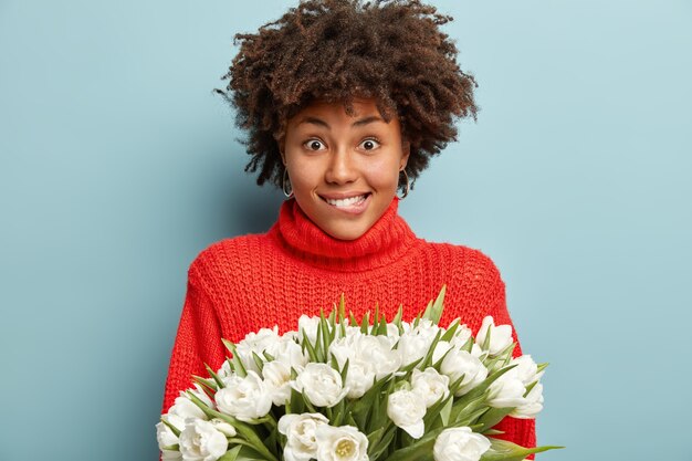 Giovane donna con capelli ricci che tiene il mazzo di fiori bianchi