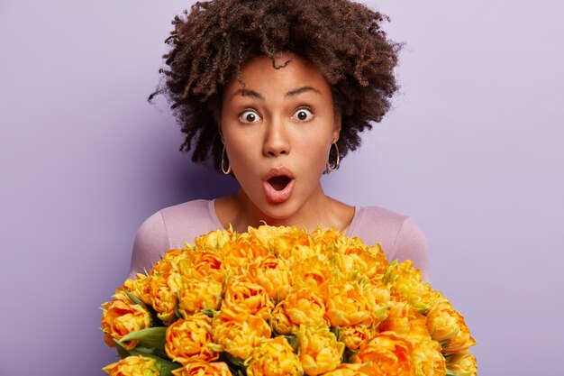 Giovane donna con capelli ricci che tiene il mazzo di fiori gialli