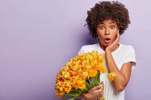 Giovane donna con capelli ricci che tiene il mazzo di fiori gialli