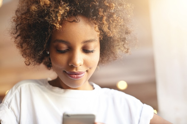 Giovane donna con capelli ricci seduti al caffè utilizzando il telefono