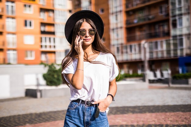 Giovane donna con cappello nero utilizzando il telefono cellulare sulla strada della città. ragazza che parla al telefono