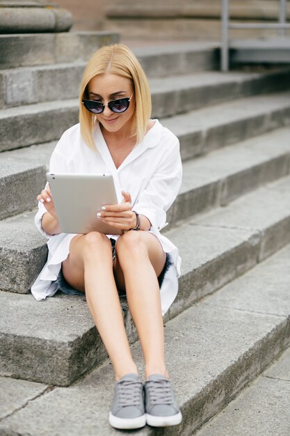 Giovane donna con computer portatile e smart phone. Bella ragazza studente che lavora al computer portatile all&#39;aperto