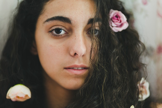 Giovane donna con fiori nei capelli che guarda l&#39;obbiettivo