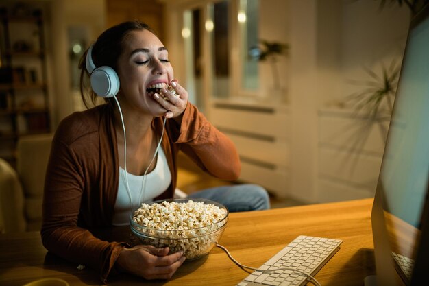 Giovane donna con gli occhi chiusi godendo mentre mangia popcorn durante la notte di cinema a casa