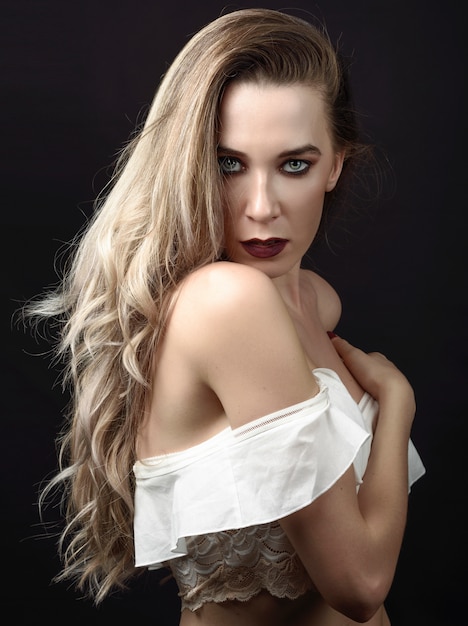 Giovane donna con i capelli lunghi e gli occhi blu su sfondo nero con make-up viola.