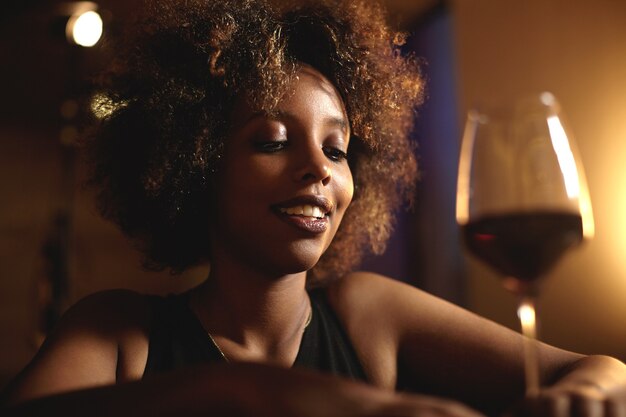 Giovane donna con i capelli ricci e un bicchiere di vino rosso