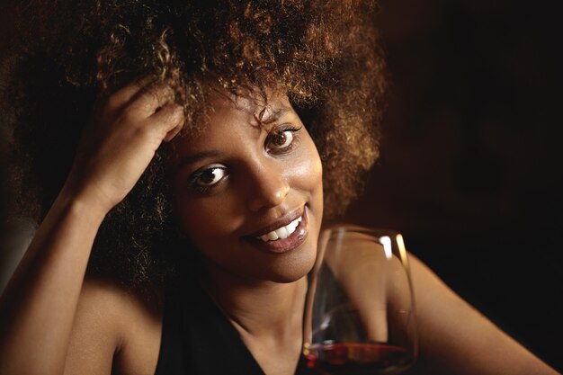 Giovane donna con i capelli ricci e un bicchiere di vino rosso