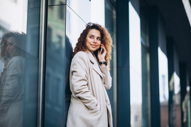 Giovane donna con i capelli ricci utilizzando il telefono in strada