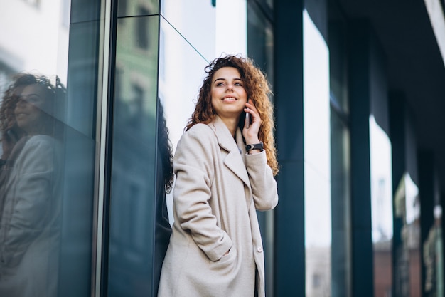 Giovane donna con i capelli ricci utilizzando il telefono in strada