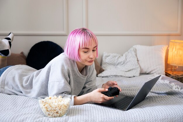 Giovane donna con i capelli rosa che gioca con un joystick sul laptop