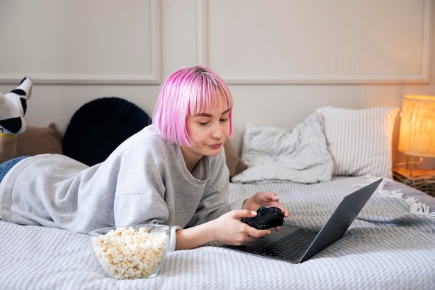 Giovane donna con i capelli rosa che gioca con un joystick sul laptop