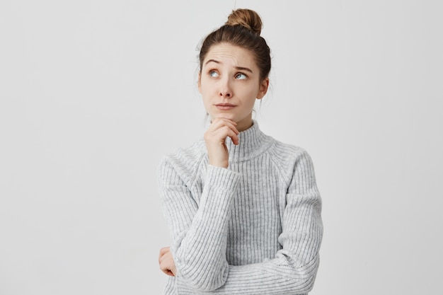 Giovane donna con i capelli scuri, tenendo il mento guardando lateralmente. Ragazza attraente che ha uno sguardo significativo al lato pensando malinconicamente al suo futuro. Concetto di obiettivi di vita