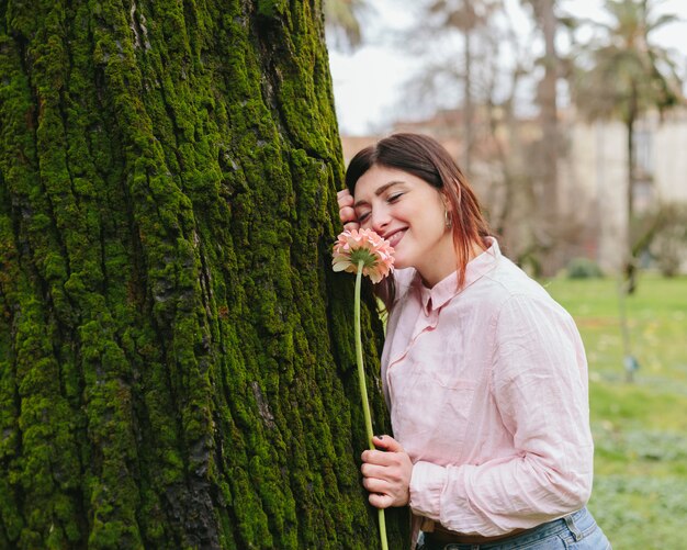 Giovane donna con il fiore che si appoggia sull&#39;albero