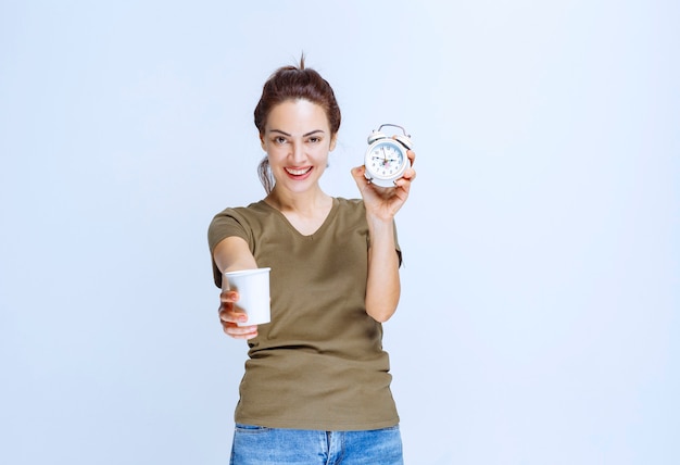 Giovane donna con in mano una sveglia e una tazza di bevanda che indica la routine mattutina