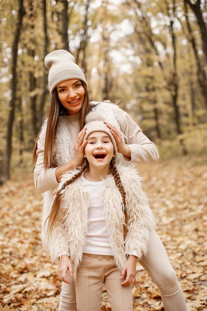 Giovane donna con la bambina che cammina nella foresta di autunno. Donna bruna gioca con sua figlia. Ragazza che indossa un maglione beige e madre che indossa abiti bianchi.