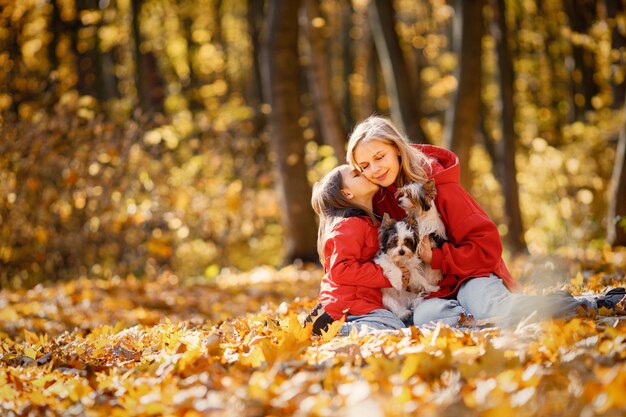 Giovane donna con la bambina che si siede su una coperta nella foresta di autunno. Una donna bionda gioca con sua figlia e tiene in mano due yorkshire terrier. Madre e figlia che indossano jeans e giacche rosse.