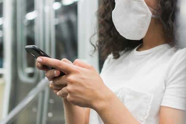 Giovane donna con la mascherina medica che controlla il suo telefono nella metropolitana