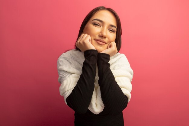 Giovane donna con la sciarpa bianca che tiene le mani sul suo viso sorridente felice e positivo