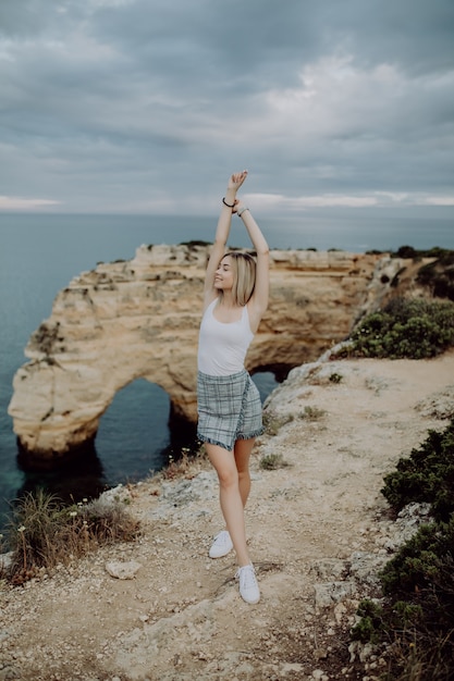 Giovane donna con le braccia spalancate in piedi sulla roccia di fronte alla spiaggia dell'oceano in Portogallo