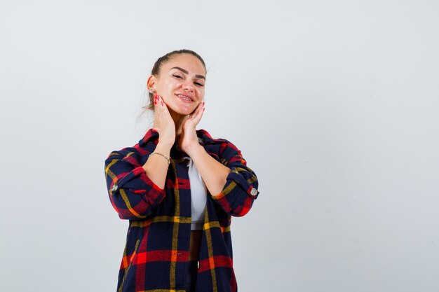 Giovane donna con le mani sul mento in alto, camicia a quadri e sguardo gioioso, vista frontale.