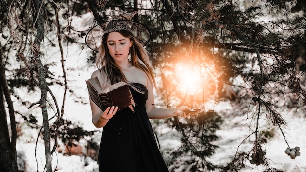 Giovane donna con libro e candela in piedi nella foresta