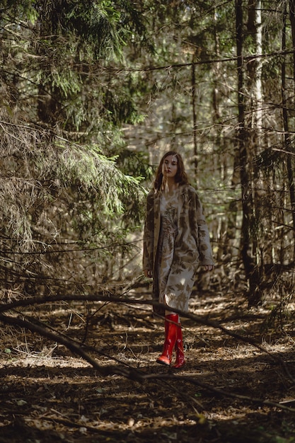 Giovane donna con lunghi capelli rossi in un vestito di lino raccolta funghi nella foresta